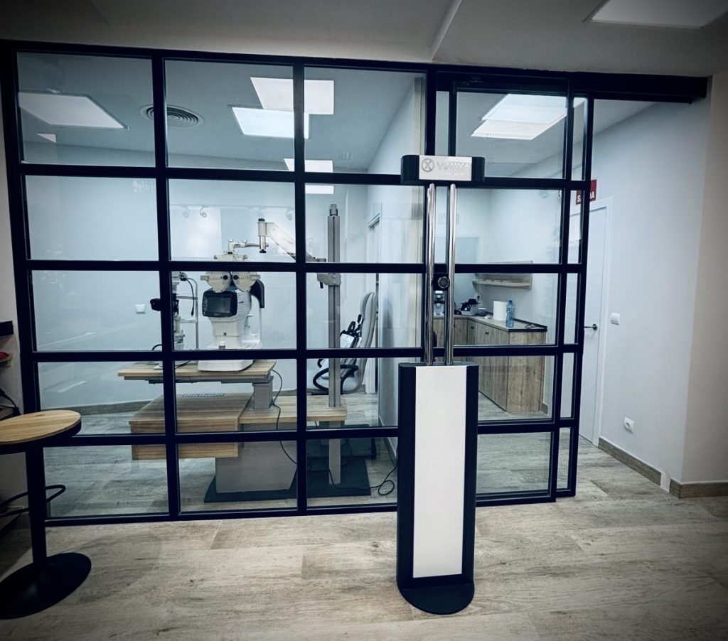 Foto del Gabinete Óptico en el local de Cámara Centro Óptico y Auditivo Montecarmelo, donde tras el cerramiento en cristalería industrial se ve la silla de graduación.